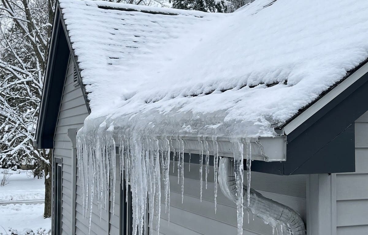 Ice dam ridge and icicles built up along the gutter and fascia line of a snow-covered New York home